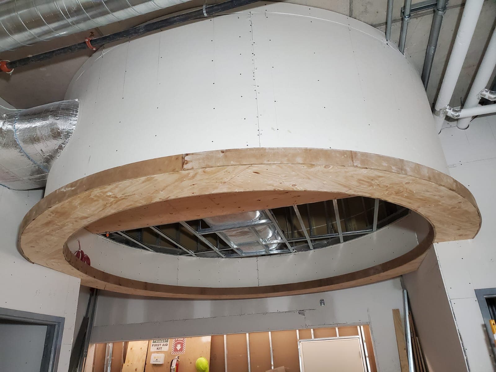 Curved drywall bulkhead suspended below an exposed ceiling